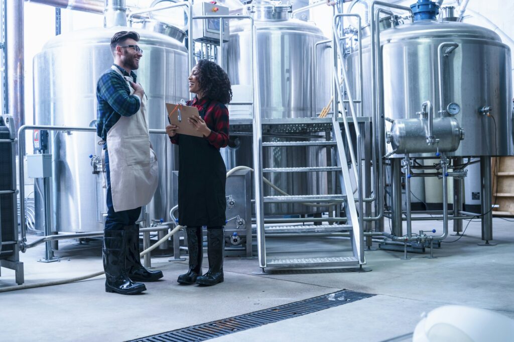 Colleagues in brewery holding clipboard face to face smiling